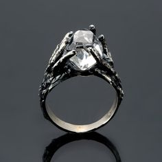 a silver ring with a stone in the center and leaves around it, on a black surface