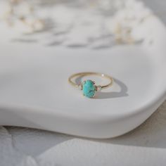 a gold ring with a turquoise stone sits on top of a white plate next to pearls