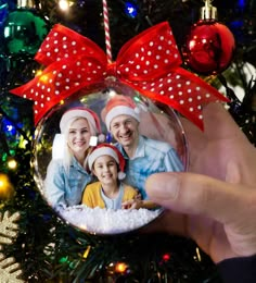 a hand holding a christmas ornament in front of a tree