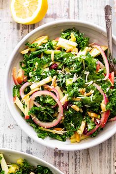 two white bowls filled with salad on top of a wooden table next to lemon wedges