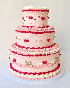 a three tiered cake with hearts and pearls on the top is pink, red and white