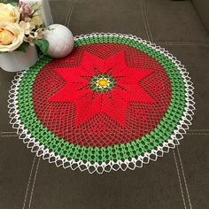 a crocheted doily with a red flower on the floor next to flowers