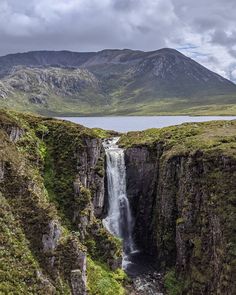 a waterfall in the middle of a mountain range with water running down it's sides