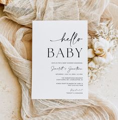 a white card with the word hello baby on it next to flowers and sheer fabric