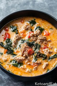 a bowl of soup with meat, spinach and tomatoes in it on a table