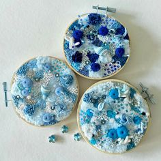 three embroidery hoops with blue and white designs on them, one is made out of buttons