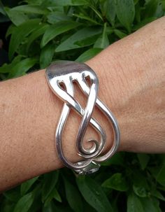 a person's arm with a silver bracelet on it and green leaves in the background