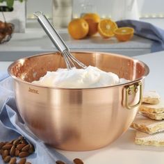 a copper bowl filled with whipped cream next to sliced oranges and almonds on a table