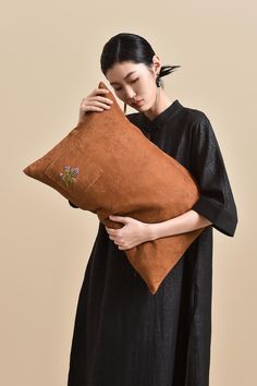 a woman holding a brown pillow with flowers on the front and side, while wearing a black dress