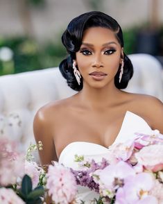 a woman sitting on a couch with flowers in front of her and wearing large earrings