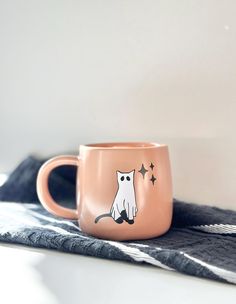 a pink coffee mug with a cat on it sitting on a black and white towel