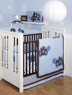 a white crib with a blue and brown turtle quilt on the bedding, next to a wooden floor