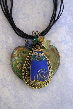 a necklace with a blue and green cat on it's back hanging from a black cord