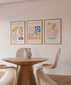 two framed pictures hang on the wall above a dining room table with chairs and vase