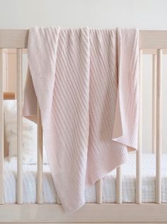 a baby's crib with a pink blanket hanging from the side of it