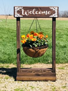 a welcome sign hanging from a wooden frame with flowers in the basket on it's side