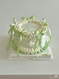 a white cake with green ribbons and bows on the top is sitting on a plate