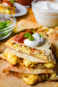 a stack of quesadillas on a cutting board with sour cream in the background