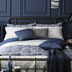 a bed with blue sheets and pillows in a room that is painted dark blue,