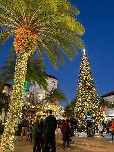 people are standing around in front of a christmas tree at the shopping center with lights on it