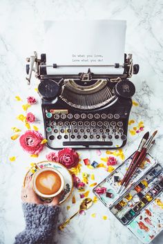 an old fashioned typewriter sitting on top of a table next to flowers and pens