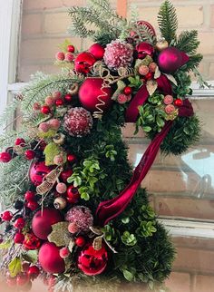 a christmas wreath with red ornaments and greenery hanging on a window sill in front of a brick wall