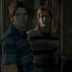 two young men standing next to each other in a dark room with one looking at the camera