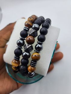 This unique set is the perfect Father's Day gift, combining three powerful stones known for their protective and grounding properties. Each bracelet is meticulously handcrafted, offering a stylish and versatile accessory that enhances any outfit, from casual to formal. The Black Onyx beads provide a sleek, matte finish that exudes elegance and strength. The Tiger's Eye beads add a touch of warmth and sophistication with their rich, golden hues, symbolizing courage and confidence. The Hematite beads, with their metallic luster, bring a modern and bold touch, known for their grounding and balancing energies. This bracelet set is strung on a durable elastic cord, ensuring a comfortable and secure fit for all wrist sizes. Whether worn individually or stacked together, these bracelets make a po Stones Meanings, Male Bracelets, Hematite Jewelry, Mens Bracelets, Lava Stone Bracelet, Birthday Flyer, Metallic Luster, Men Bracelet, Diy Bracelets Patterns