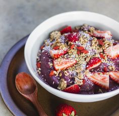 a bowl filled with fruit and granola on top of a plate next to a spoon