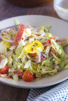 a white plate topped with salad on top of a wooden table next to a fork