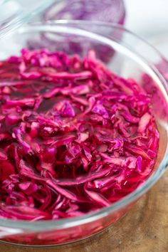 a glass bowl filled with red cabbage on top of a wooden table