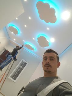 a man standing on a ladder in front of a ceiling with clouds painted on it