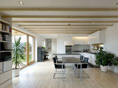 a large open kitchen and dining room area with wood flooring, white walls and ceiling beams