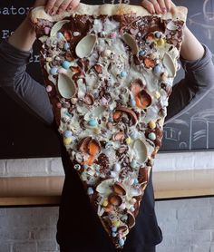 a person holding up a large slice of pizza with chocolate and candy toppings on it