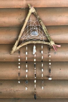 a piece of driftwood hanging from the side of a building with beads and stones attached to it