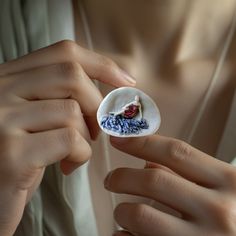 a woman is holding a button with a small bird on it's side and wearing a white shirt