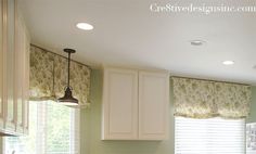 a kitchen with white cabinets and counter tops next to a window covered in valance