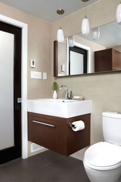 a white toilet sitting next to a bathroom sink under a mirror above a wooden cabinet