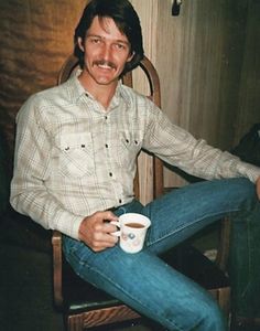 a man sitting in a chair with a cup of coffee on his lap and smiling at the camera