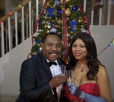 a man and woman pose for a photo in front of a christmas tree