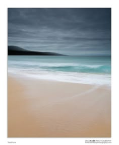 an ocean scene with waves crashing on the beach and mountains in the distance, under a cloudy sky