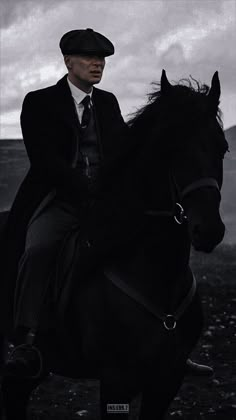 a man riding on the back of a black horse next to a field and cloudy sky