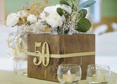 a wooden box filled with flowers and candles on top of a white table cloth covered table