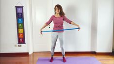 a woman standing on top of a purple mat holding a blue hula hoop