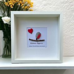 a white frame with a red bird and two hearts on it next to some yellow flowers