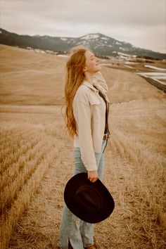 a woman standing in the middle of a field with her hat up to her chest