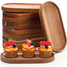 three cupcakes with fruit on top sit in front of a wooden box