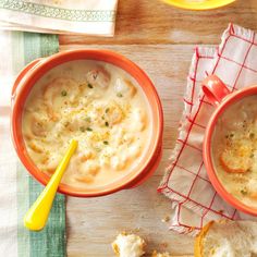 two orange bowls filled with soup on top of a wooden table next to some bread