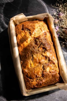 a loaf of bread sitting in a pan on top of a black table next to dried herbs