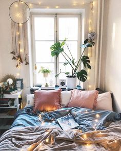 an unmade bed with lots of pillows and lights in the window sill above it